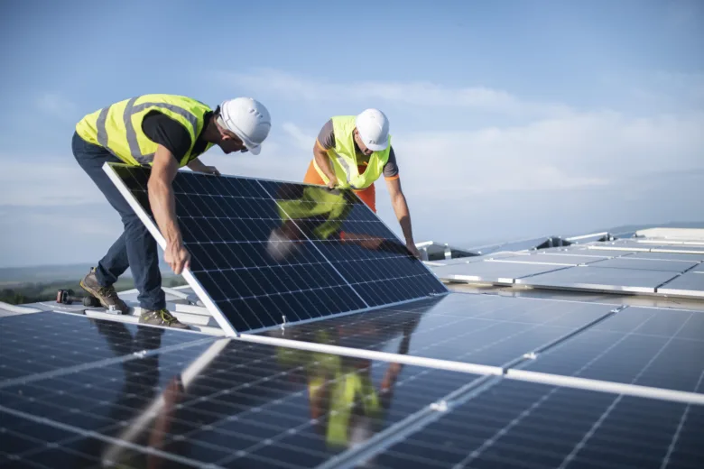 Dva dělníci montují fotovoltaickou desku na střechu.