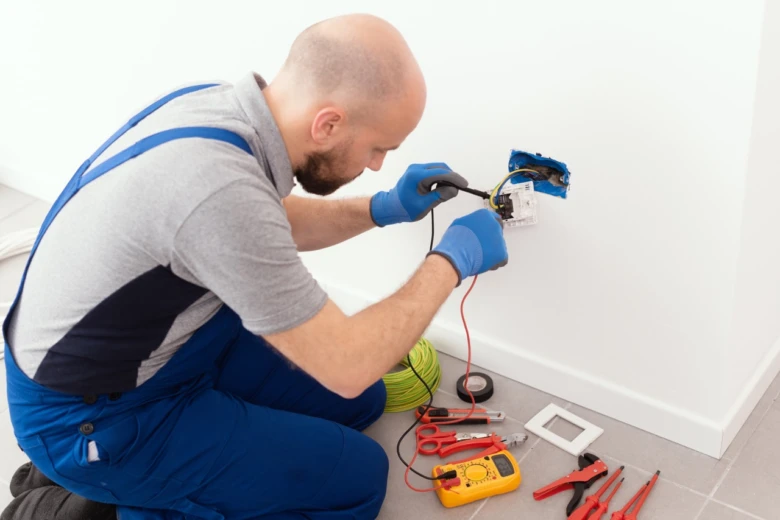 Elektrikář testuje instalaci v zásuvce s multimetrem.