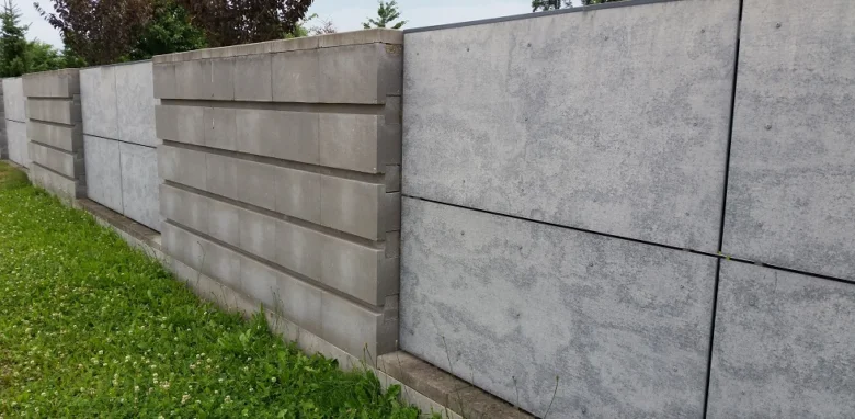 Řada šedých betonových panelů tvořících zadržovací zeď na trávníku.