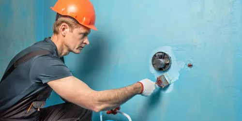 Montér aplikuje hydroizolační hmotu kolem elektrické zásuvky v koupelně.