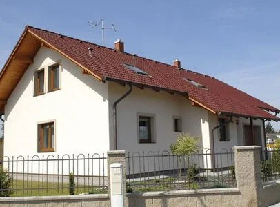 Bílá fasáda domu s červenou taškovou střechou.