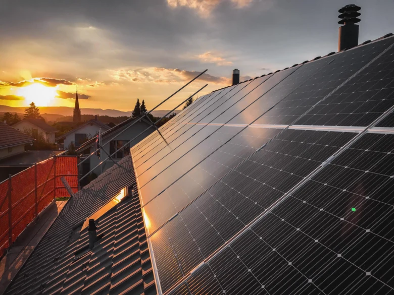 Fotovoltaické panely na střeše rodinného domu při západu slunce.