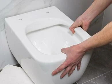 Ruce instalují bílý záchod do koupelny.