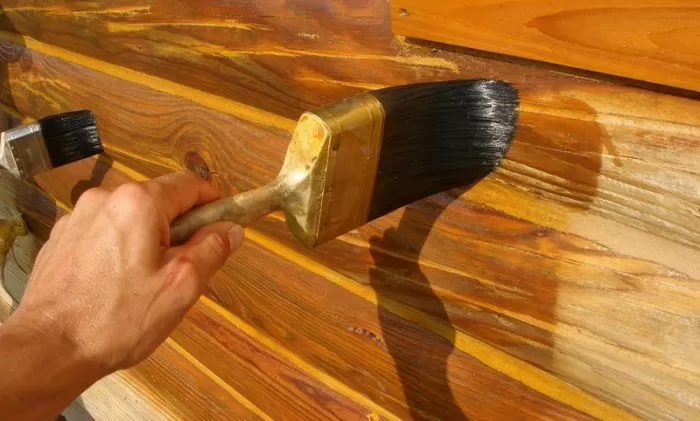 Ruční nanášení venkovní lazury na dřevěné prkno štětcem.
