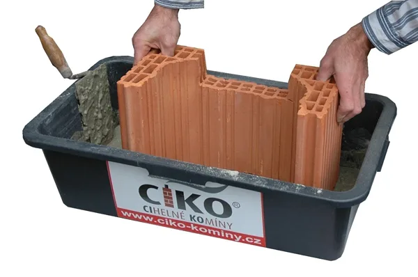 Ruční montáž prázdných cihel komína v kontejneru s maltou.