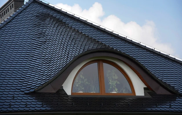 Detail vikýře na střeše s taškami a obloukovým oknem.