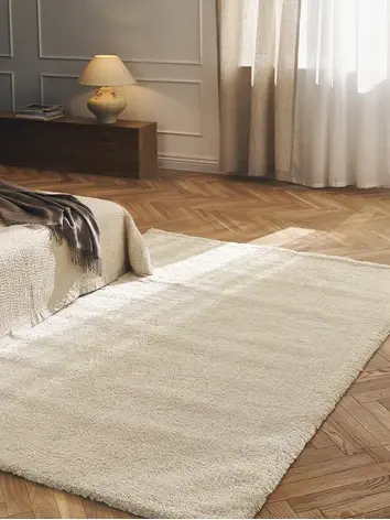 Béžový koberec v obývacím pokoji s postelí, stolní lampou a okny za závěsem.