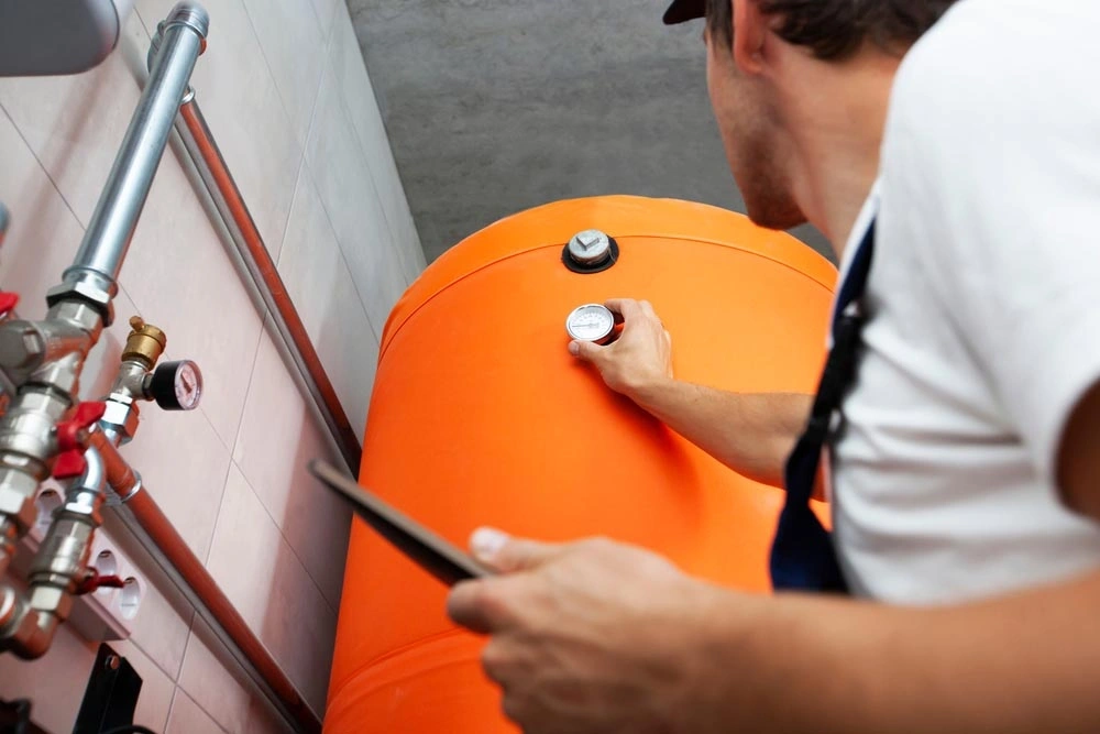 Technik kontroluje oranžovou akumulační nádrž na teplou vodu.