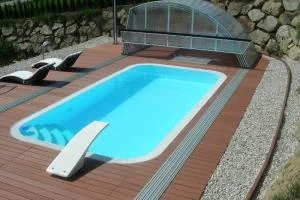 Polozapuštěný bazén s dřevěnou terasou a lehátky.