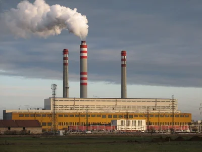 Velká elektrárna spalující uhlí s kouřem z komínů na pozadí oblohy.