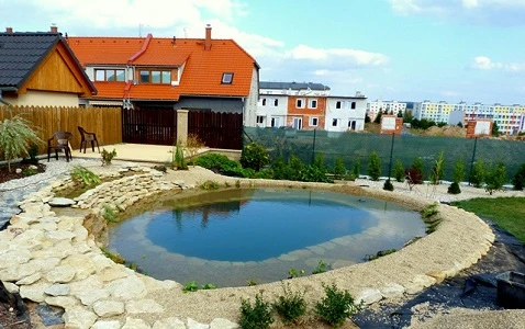 Hotový koupací jezírko s kamenným obvodem v zahradě.