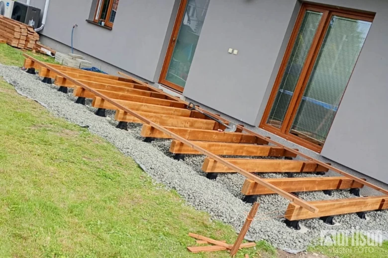 Stavba dřevěné terasy: montáž nosníků na štěrbinu u domu.