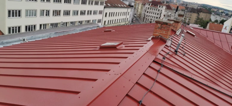 Červená plechová střecha s okny a komínem po klempířských pracích.