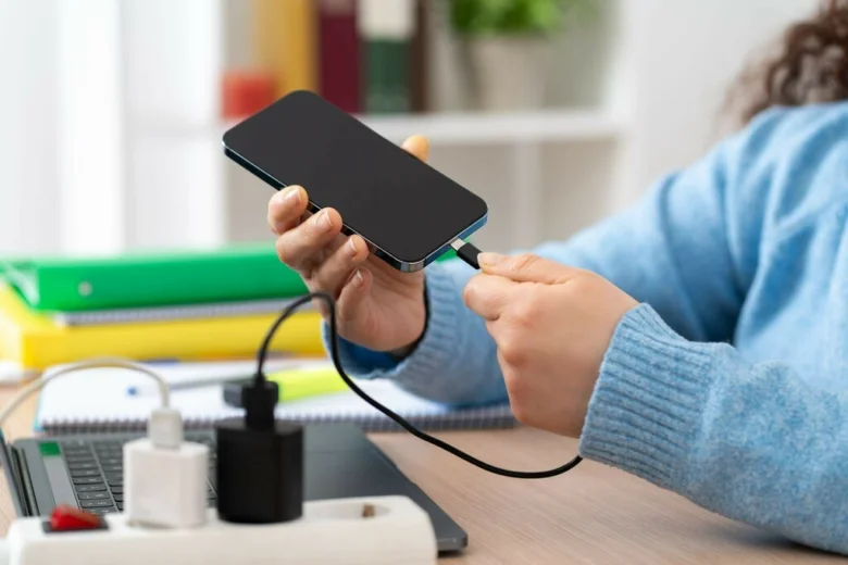 Osoba připojuje nabíjecí kabel k chytrému telefonu na pracovním stole.
