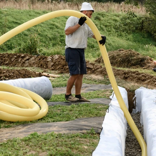 Muž instaluje žluté drenážní trubice do příkopu pro odvodnění pozemku.