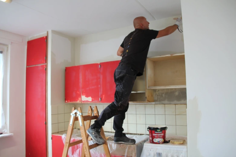 Muž maluje červené kuchyňské skříňky na schodišti.