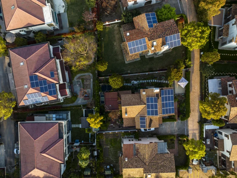 Vzdušný pohled na rodinné domy s fotovoltaickými panely na střechách.