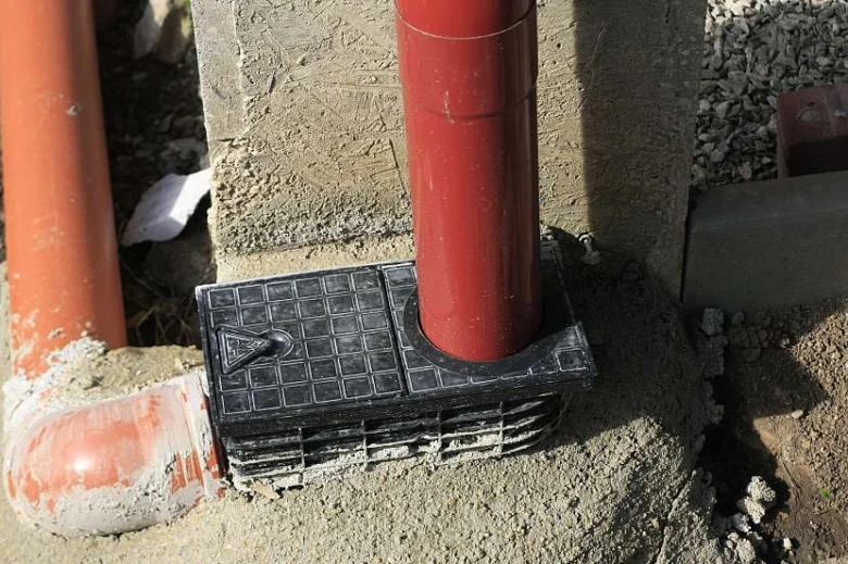 Černý plastový základ pro okapovou svodnici nainstalovaný na červené rourě.