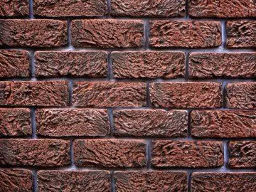 Detailní pohled na červenohnědou cihlovou zeď s viditelnými spárami.
