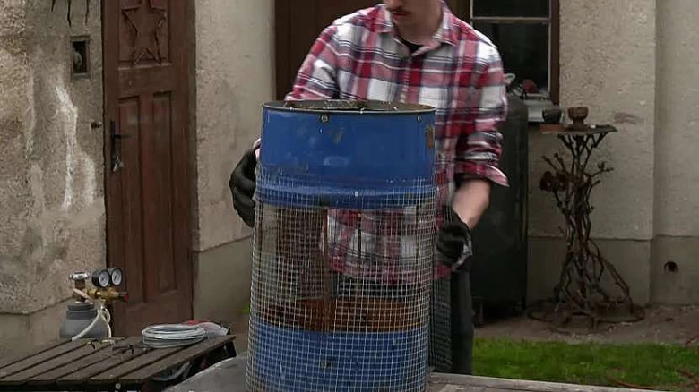 Muž prosévá zeminu pomocí modrého barelu s mříží.