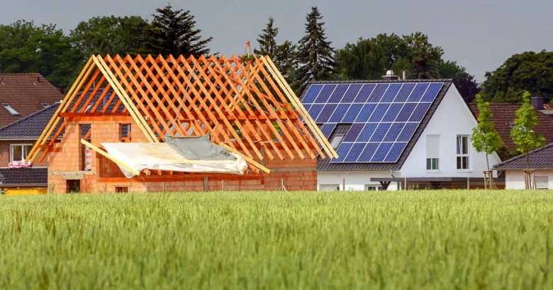 Dům s fotovoltaickými panely vedle stavby v zeleném poli.