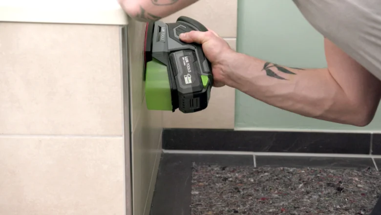 Muž nanáší tmel na dlažbu v koupelně pomocí elektrického nástroje.