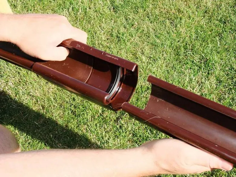 Ruka drží hnědý plastový okap na trávníku.