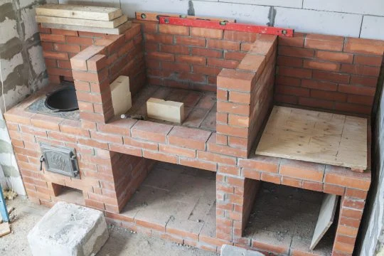 Částečně postavený cihlový zahradní gril s více komorami.