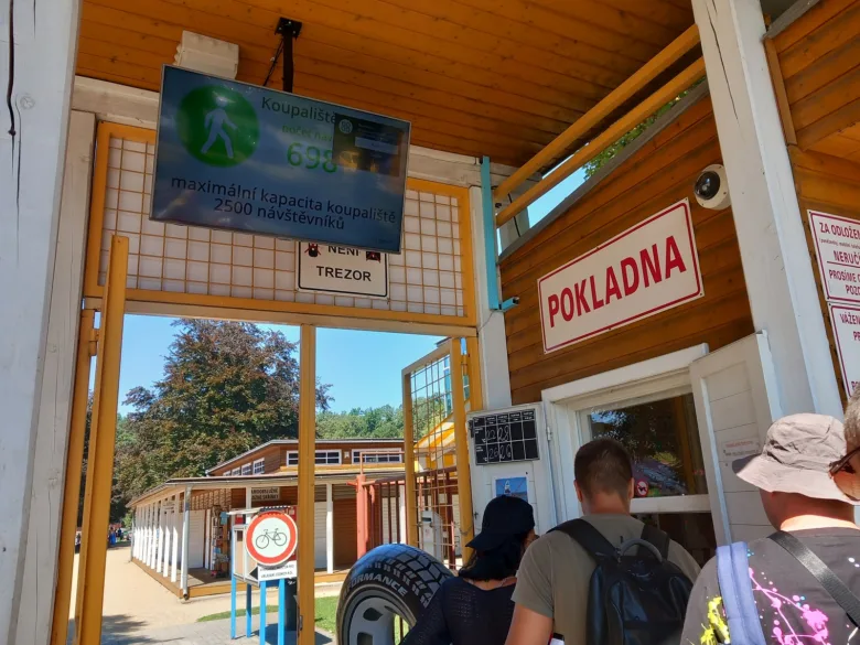 Vstup do koupaliště s tabulkou kapacity a pokladnou.