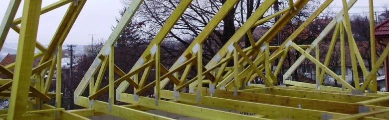 Žluté dřevěné vazníky pro střechu v procesu montáže.