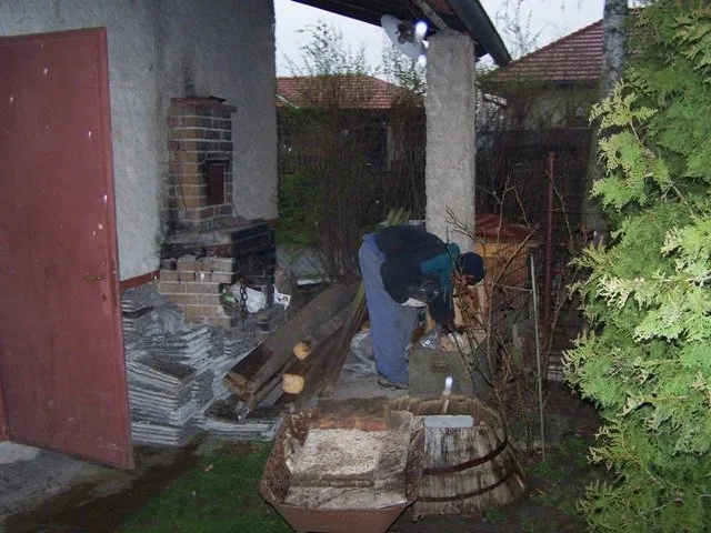 Člověk staví dřevěnou pergolu u domu s použitím cihel a trámů.