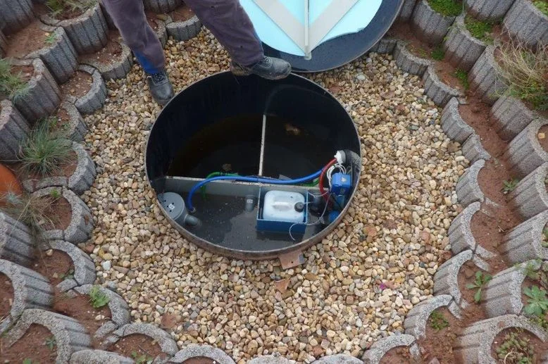 Instalace domácí čistírny odpadních vod v zahradě s kamením.