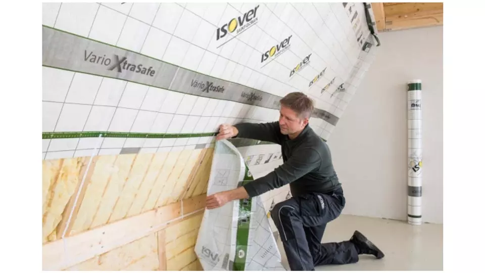 Muž instaluje nadkrokevní hydroizolační fólii na dřevěnou konstrukci.