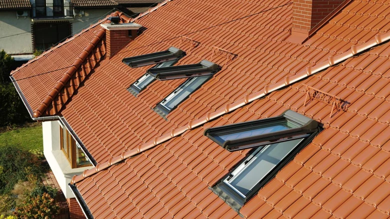 Polovalbová střecha s valbami, okapy a světlíky na červené tašce.