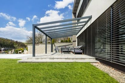 Moderní kovová pergola nad venkovním posezením u domu.