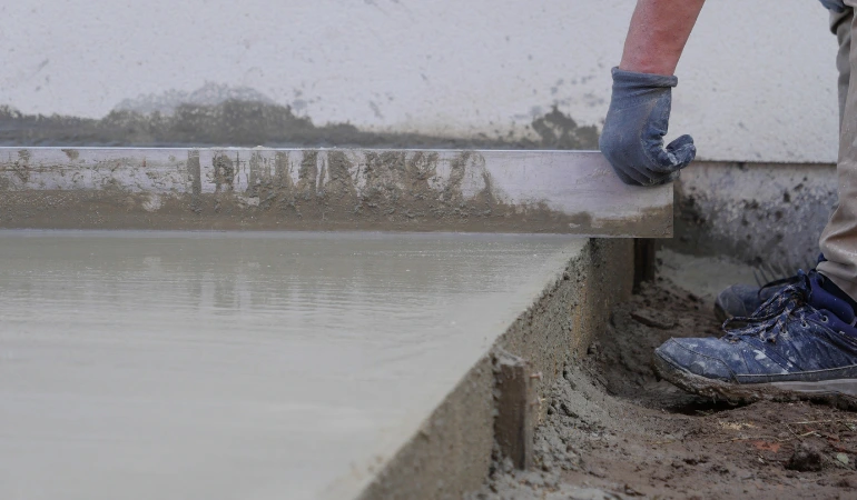 Stavebník vyrovnává čerstvý beton pro terasu u domu.