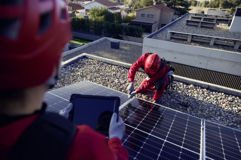 Dva pracovníci montují fotovoltaické panely na střechu domu.
