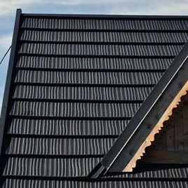 Detail tmavé plechové střešní krytiny s hřebenem.