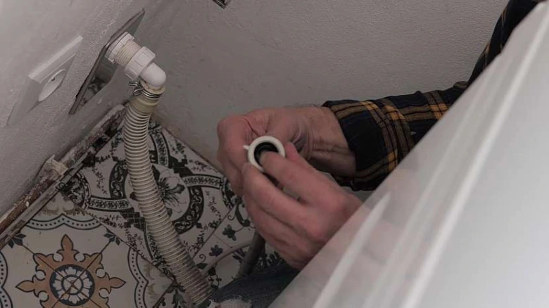 Ruka drží plastový spoj pro hadici pračky na odpad.