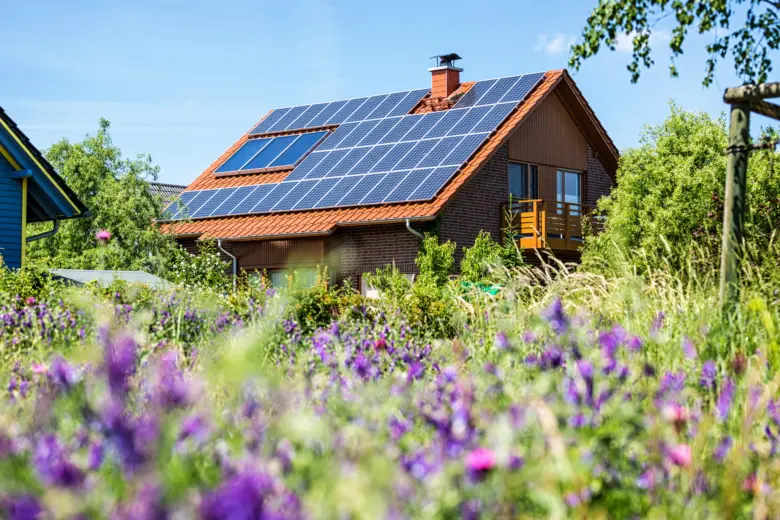 Dům s fotovoltaickými panely na střeše v zahradě.