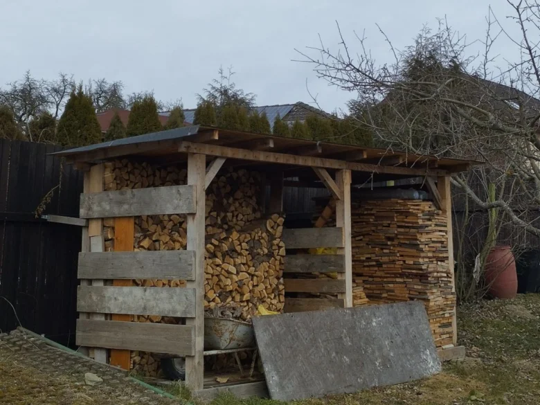 Dřevník s dřívím postavený z palet a trámů.