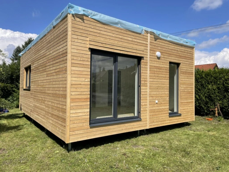 Moderní dřevěný modulární dům na trávníku pod modrou oblohou.