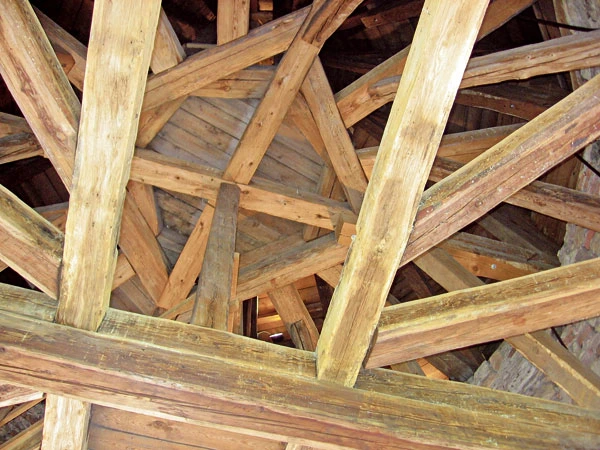 Detail dřevěných střešních kroků s křížícími se trámy.