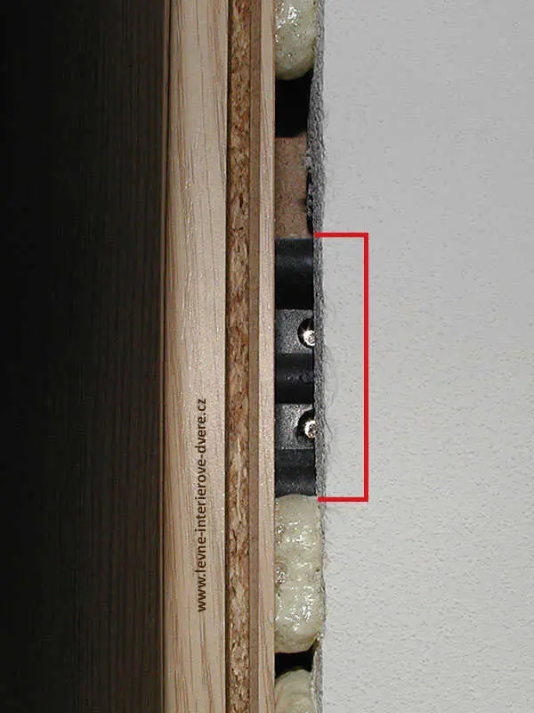 Detailní pohled na montáž zárubně dveří do otvoru s expandovanou pěnou.