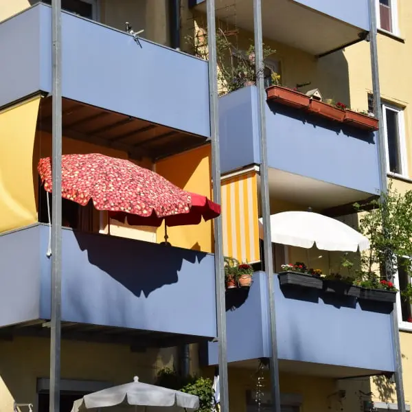 Balkony panelového domu s různými způsoby zastínění včetně střešních plachet.