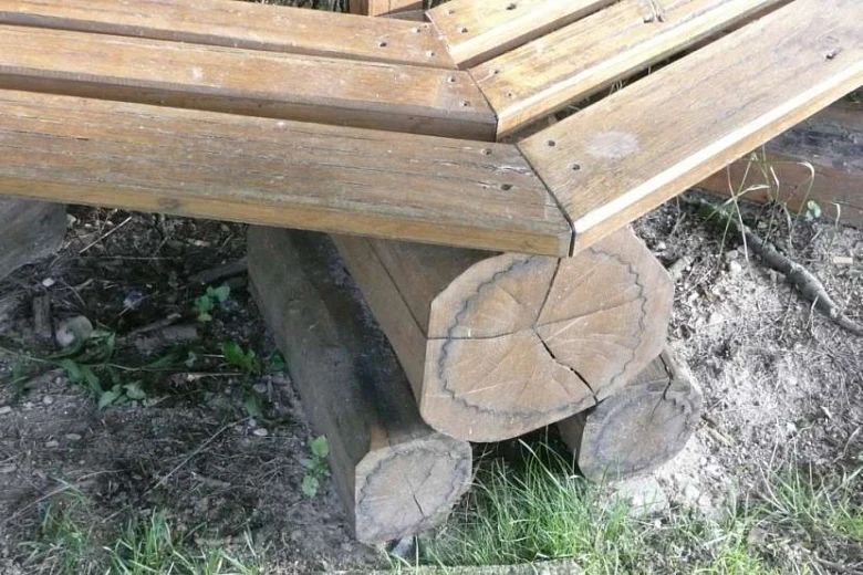Dřevěná lavice postavená na kmenových nohách venku.