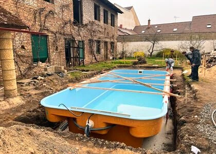 Modrý nadzemní bazén se instaluje v příkopu vedle staré budovy.