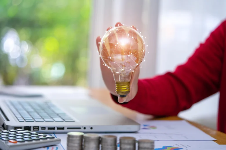 Ruka drží svítící žárovku s digitální mřížkou nad finančními nástroji.