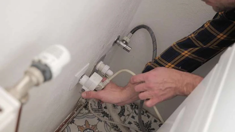 Muž připojuje vodovodní hadice k ventilu pračky.