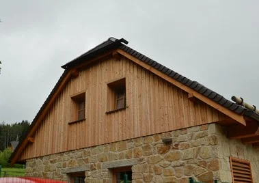 Dům s kamennou spodní částí a dřevěnou provzdušňovanou fasádou.